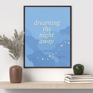 Pode incluir: Uma impressão artística emoldurada com as palavras "dreaming the night away" em uma fonte caprichosa contra um fundo de céu azul com formas de nuvens e estrelas. Um vaso marrom com plantas secas e uma pilha de livros estão em uma prateleira de madeira.