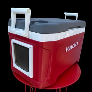 May include: Red Igloo cooler with a white lid and a white door with a clear window. The cooler has two white handles on the top and a white handle on the side. The cooler is sitting on a red table with three legs.