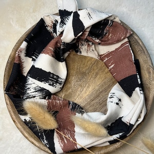 Könnte beinhalten: Ein weißes, schwarzes und braunes gemustertes Stoffhaarband mit einem geknoteten Design. Das Haarband liegt in einer Holzschale.