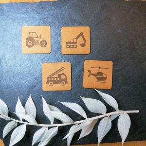 Könnte beinhalten: Vier Holzkästen mit verschiedenen Fahrzeugillustrationen. Die Kästen sind braun mit schwarzen Umrissen und schwarzen Fahrzeugsilhouetten. Die Fahrzeuge sind ein Traktor, ein Bagger, ein Feuerwehrauto und ein Hubschrauber.