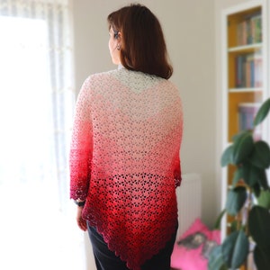 May include: A woman wearing a crocheted shawl with a gradient of red, pink, and white colors. The shawl is made with a delicate openwork pattern.