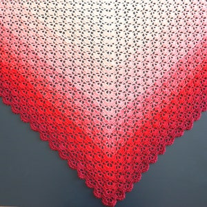 May include: A crocheted shawl with a gradient of red, pink, and white. The shawl is triangular in shape and has a scalloped edge.