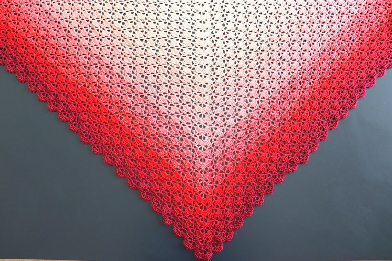 May include: A crocheted shawl with a gradient of red, pink, and white. The shawl is triangular in shape and has a scalloped edge.