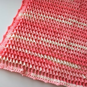 May include: A pink and white crocheted blanket with a diamond pattern. The blanket is made with a soft yarn and has a delicate, lacy look.