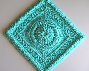 May include: A turquoise crochet square with a detailed center design. The square has a border with a repeating pattern.