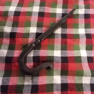 May include: A black metal hook with a twisted design. The hook is on a red and green plaid fabric.