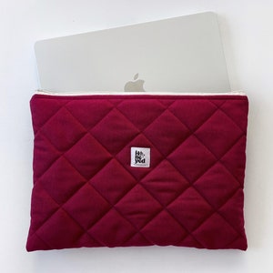 Peut inclure: Une housse d'ordinateur portable matelassée de couleur bordeaux foncé avec une fermeture éclair blanche et une petite étiquette noire qui dit "Hello Yeti".