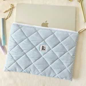 Può includere: Una custodia per laptop trapuntata a righe blu e bianche con un piccolo logo bianco e nero che dice "Hey You".