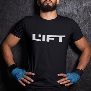 May include: A man wearing a black t-shirt with the word "LIFT" printed in white on the front. He is wearing blue wrist wraps and has his hands on his hips.