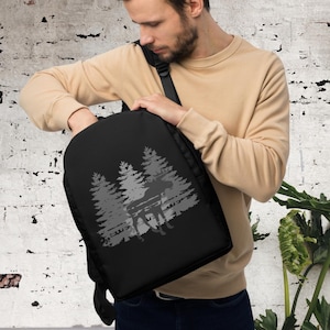 May include: A black backpack with a gray moose and pine tree design. The backpack has a zipper closure and adjustable straps.