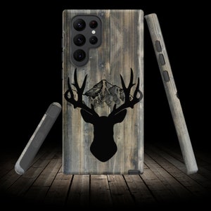 May include: A phone case with a rustic wood grain design featuring a silhouette of a deer with antlers and a mountain range. The case is designed for a Samsung Galaxy S21 Ultra.