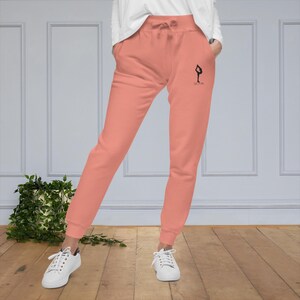 May include: A pair of coral pink sweatpants with a black graphic of a person doing a yoga pose and the word "CALM" printed on the right leg.