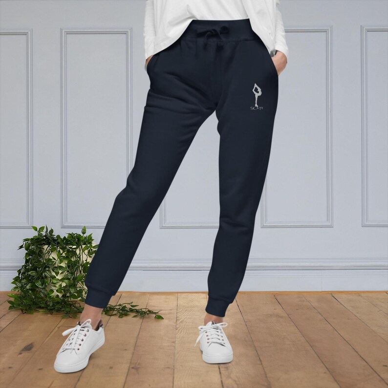 May include: Navy blue sweatpants with a white graphic of a person doing a yoga pose and the text "Na Mas Te".