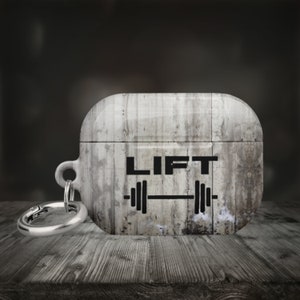 May include: A gray and white Airpods case with a keychain. The case has a distressed concrete look and the words "LIFT" and a weightlifting barbell graphic printed on it.