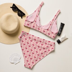 Puede incluir: Conjunto de bikini de dos piezas con estampado de flamencos rosas. El top y la braguita de cintura alta se muestran con un sombrero de paja, gafas de sol, protector solar y una concha. El bikini es de tejido suave.