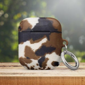 May include: A brown, black and white cow print silicone case for AirPods with a silver metal carabiner.