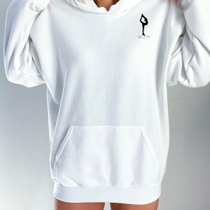 May include: White oversized hoodie with a black silhouette of a figure ice skating and the word "SKATE" printed on the front.