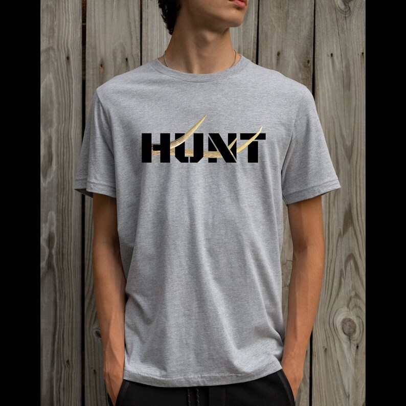 May include: A heather gray t-shirt with the word "HUNT" in black block letters. The letter "U" is replaced with a gold-colored antler design, and a gold antler design is also on the right side of the letter "T".