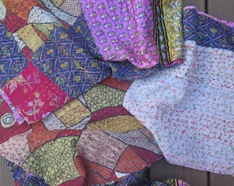May include: A patchwork textile with a variety of patterns and colors. The fabric features squares of red, blue, yellow, and purple, with floral and geometric designs. The textile is likely a quilt or decorative fabric.