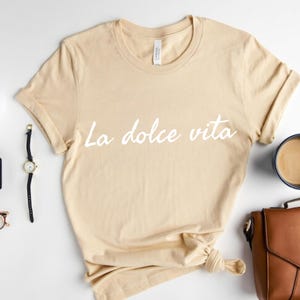 May include: A beige t-shirt with the text "La dolce vita" printed in white on the front.