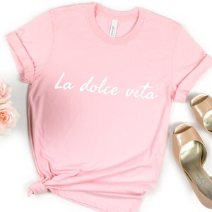 May include: A pink t-shirt with the text "La dolce vita" in white lettering.