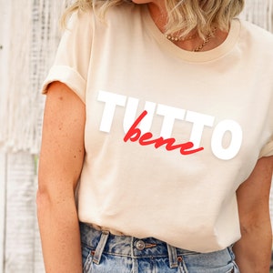 May include: A beige t-shirt with the words "TUTTO bene" printed in white and red.