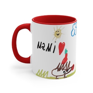 Puede incluir: Taza de cer&aacute;mica blanca con borde y asa rojos. La taza presenta un dibujo infantil de un sol, una nube, un coraz&oacute;n y un erizo. El dibujo tambi&eacute;n incluye el texto "MAMI" en marcador negro.