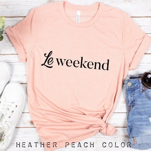 May include: A heather peach colored t-shirt with the text "Le weekend" in black script.