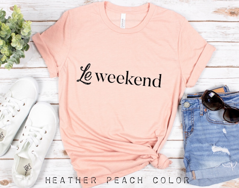 May include: A heather peach colored t-shirt with the text "Le weekend" in black script.