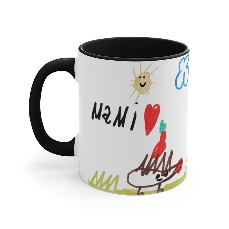 Puede incluir: Taza de caf&eacute; de cer&aacute;mica blanca con asa y borde negros. La taza presenta un dibujo infantil de un sol, una nube, un coraz&oacute;n y la palabra "MAMI" en marcador negro. El dibujo es de un erizo rojo y verde con un coraz&oacute;n rojo en la cabeza.