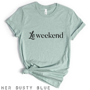 May include: A heather dusty blue t-shirt with the text "Le weekend" in black cursive lettering.