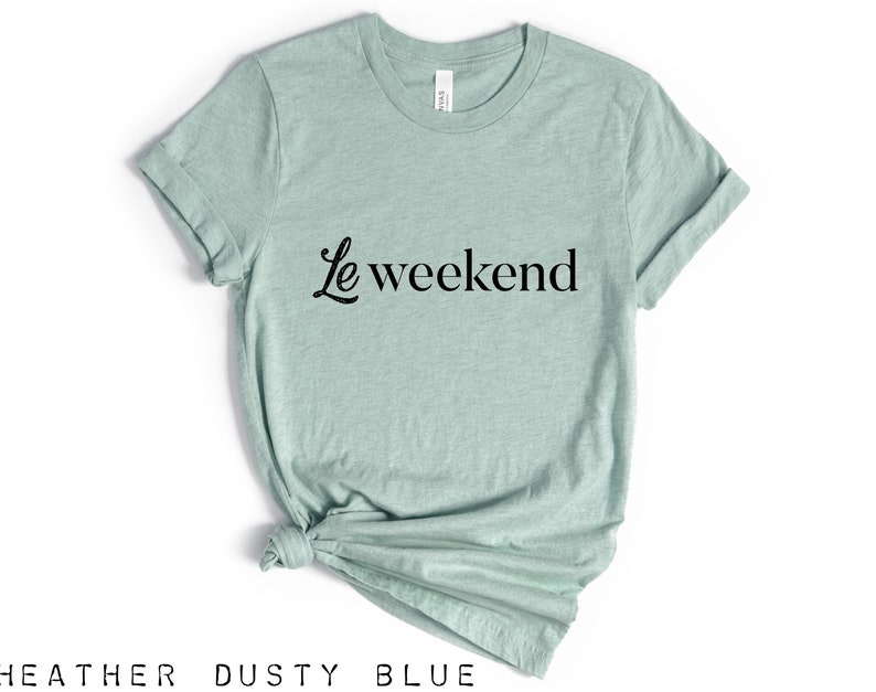 May include: A heather dusty blue t-shirt with the text "Le weekend" in black cursive lettering.