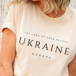 Pu&ograve; includere: Una maglietta color crema con la scritta "THE LAND OF FREE PEOPLE UKRAINE EUROPE" stampata in nero.