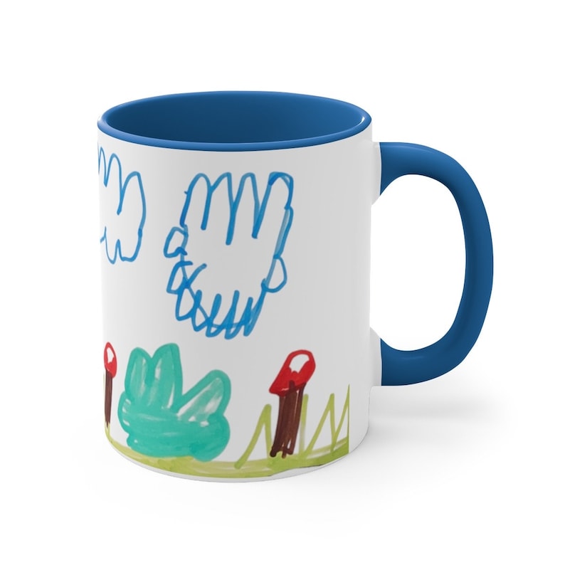 Puede incluir: Taza de cer&aacute;mica blanca con borde y asa azules. La taza presenta un dibujo infantil de un cielo azul con nubes, hierba verde y setas rojas.