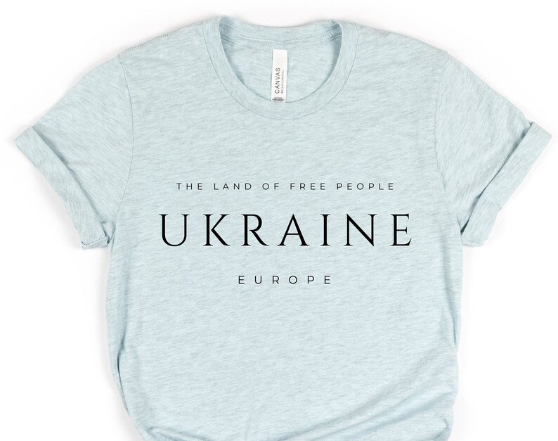 Pu&ograve; includere: Una maglietta blu chiaro con testo nero che recita "The Land of Free People, Ukraine, Europe".