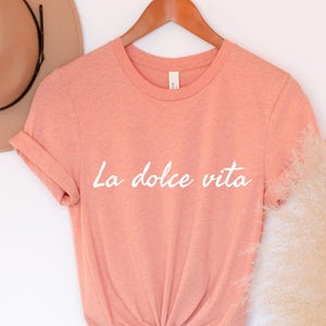 May include: A peach-coloured t-shirt with the text "La dolce vita" printed in white on the front.