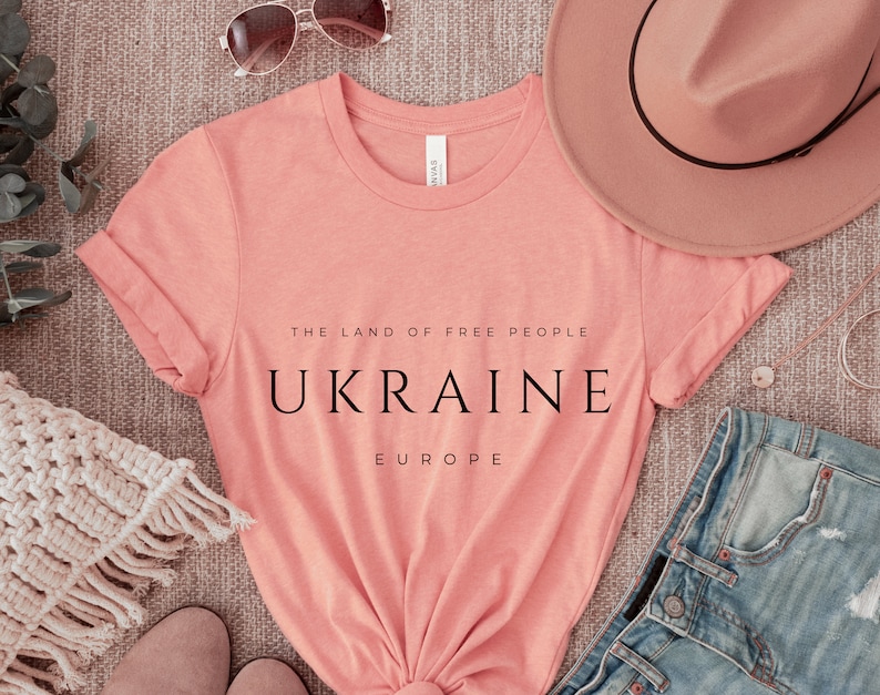 Pu&ograve; includere: Una maglietta color pesca con il testo "The Land of Free People, Ukraine, Europe" stampato in nero.