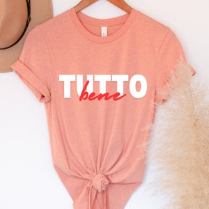 May include: A peach-colored t-shirt with the text "TUTTO bene" in white and red lettering.