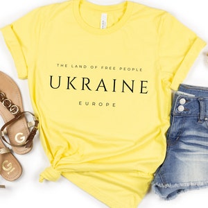 Pu&ograve; includere: Maglietta gialla con testo nero che recita "The Land of Free People, Ukraine, Europe".