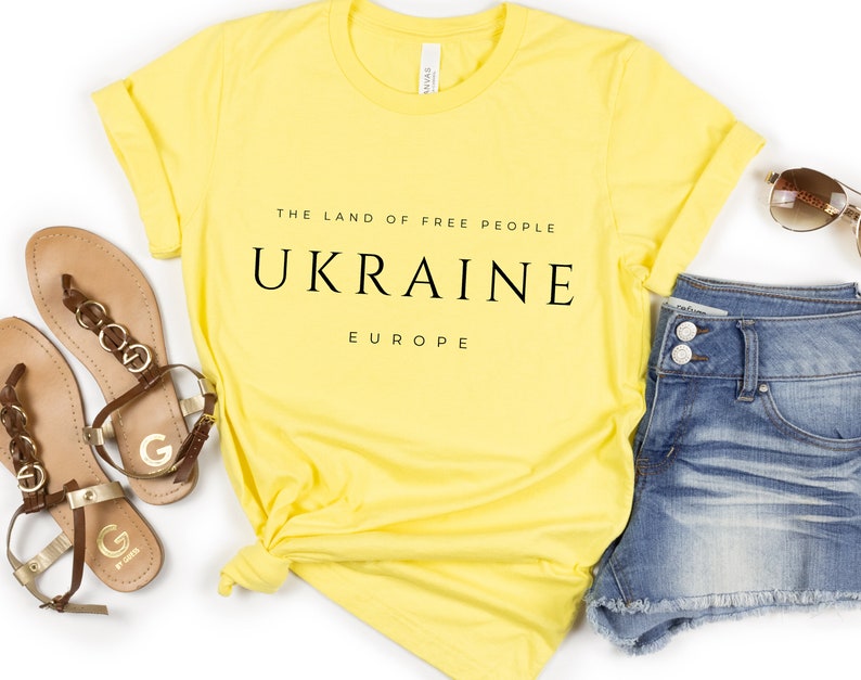 Pu&ograve; includere: Maglietta gialla con testo nero che recita "The Land of Free People, Ukraine, Europe".