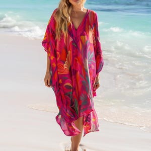 May include: A vibrant, flowing, V-neck kaftan dress in shades of pink, red, orange, and green, with a floral pattern. The dress is worn on a beach with turquoise water in the background.