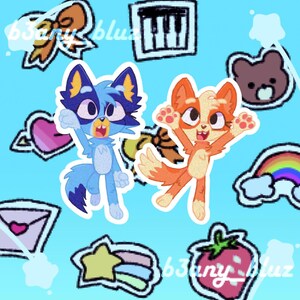 May include: A blue and white cartoon cat with a pink heart and a rainbow star sticker. A red and white cartoon fox with a rainbow sticker. Both characters are on a light blue background with other colorful stickers.