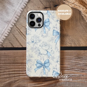 May include: A phone case with a floral and bow pattern in light blue and white. The case has a black border and a camera cutout. The text "MAGSAFE AVAILABLE" is on a round sticker. The brand name "Essence creations" is at the bottom.