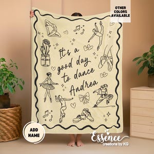 May include: Cream-colored blanket with black line art of ballet dancers, shoes, and musical notes. The text "It's a good day to dance Andrea" is displayed. The blanket has a black wavy border and is suitable for dance enthusiasts.