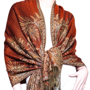 May include: A brown and gold paisley patterned shawl with fringe. The shawl is draped over a mannequin's shoulders.