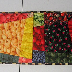 May include: A colourful patchwork table runner featuring a variety of fruits and vegetables, including red peppers, green peppers, tomatoes, cherries, blueberries, and bananas.