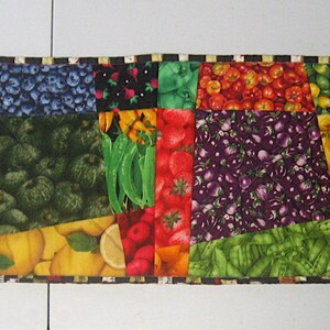 May include: A colourful table runner with a patchwork design featuring various fruits and vegetables. The runner is made of fabric and has a black and white checked border.