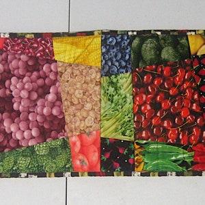 以下が含まれることがあります： 様々な果物と野菜、ブドウ、チェリー、バナナ、ブロッコリーなどがパッチワークのデザインで描かれたカラフルなテーブルランナーです。