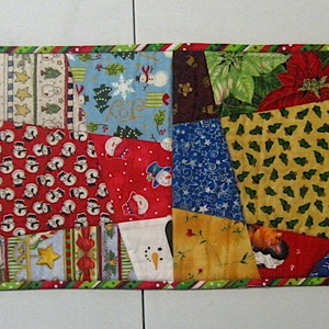 May include: A colourful patchwork table runner with a Christmas theme. The runner is made of various fabrics with different patterns, including snowflakes, holly, and snowmen. The runner is trimmed with a green and red border.