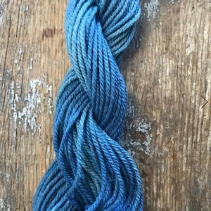 Könnte beinhalten: Ein gedrehter Strang Stickgarn mit einer variierenden Farbpalette aus tiefem Marineblau, Mittelblau und helleren Himmelblautönen. Das Garn besteht aus mehreren verzwirnten Fäden mit einer sichtbaren Textur und einem gleichmäßigen, matten Finish.